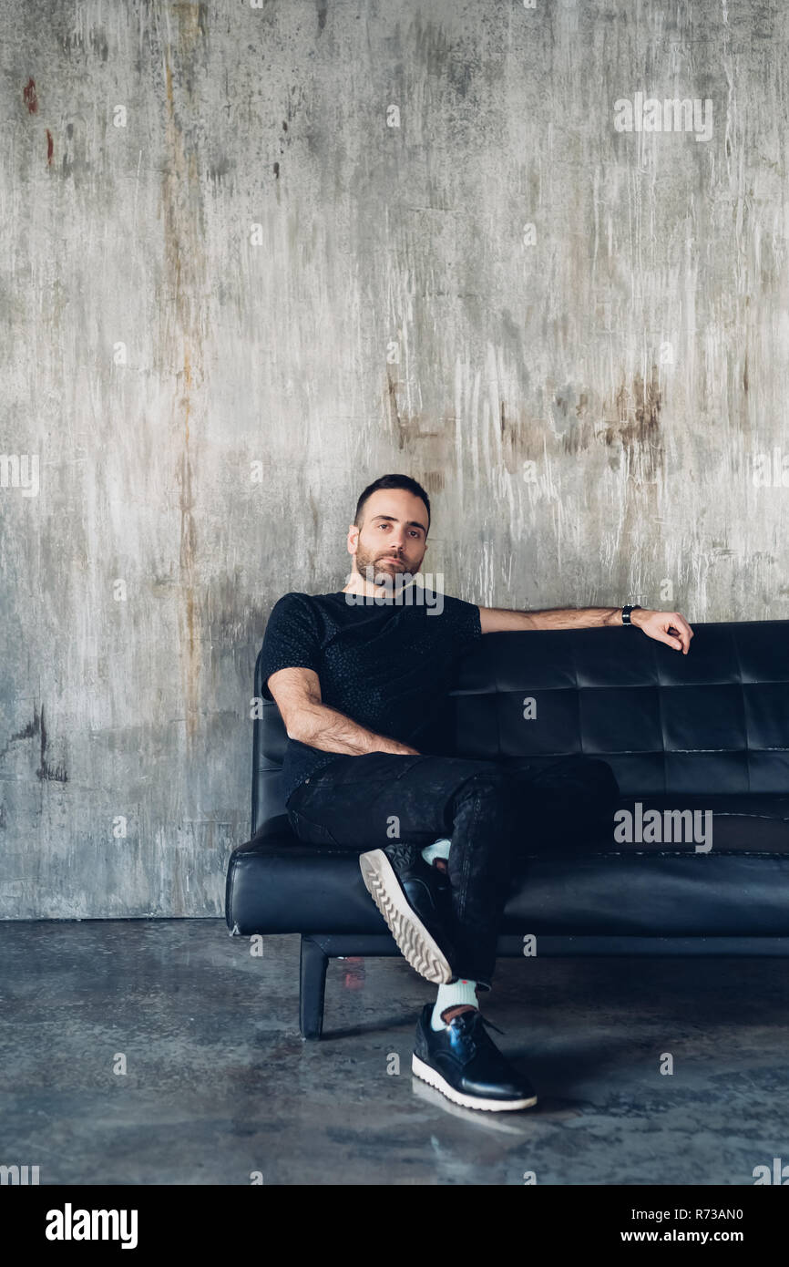 Man sitting on sofa, concrete wall in background Stock Photo