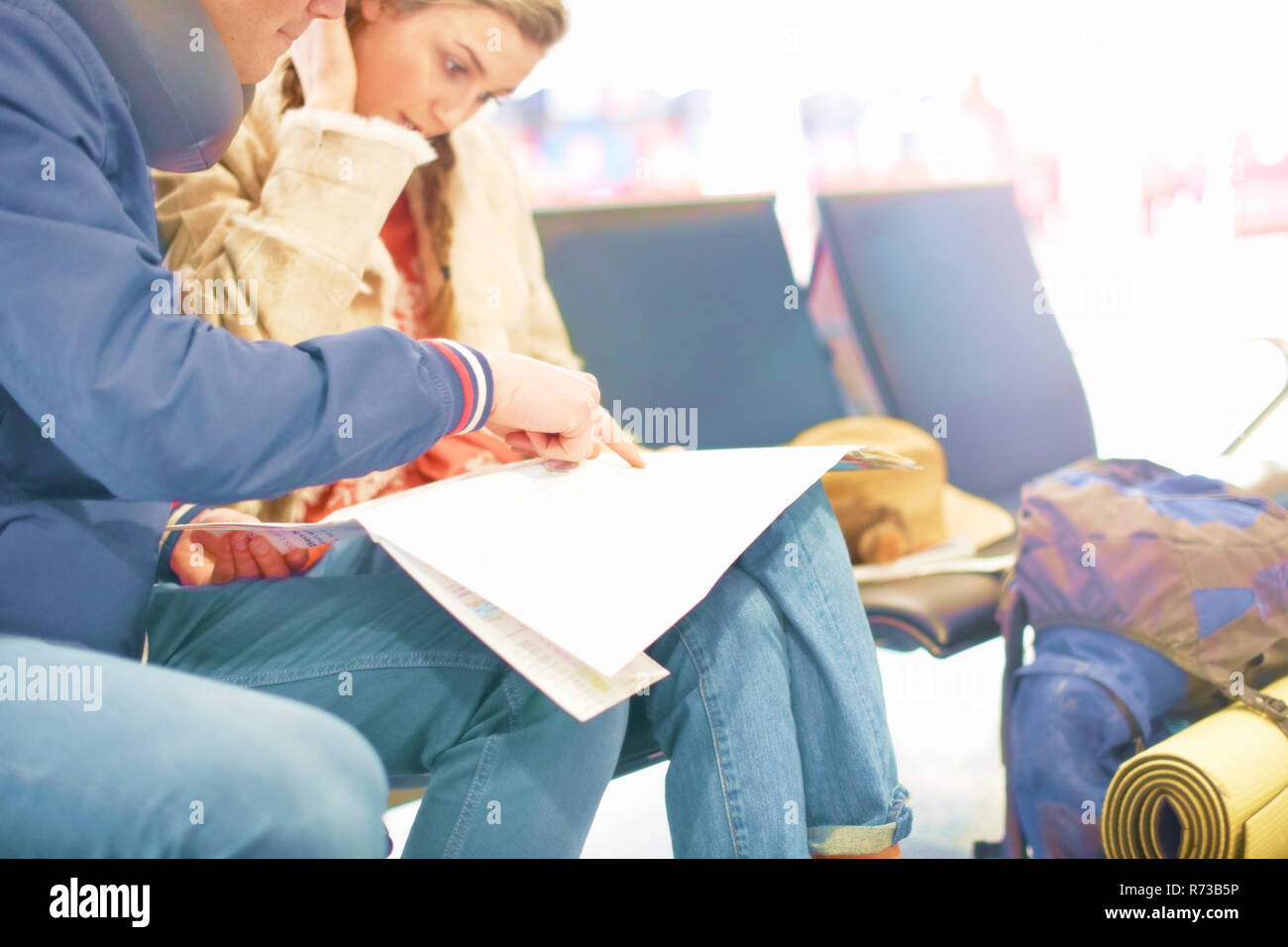 Young couple sitting in airport departure lounge, looking at map, planning trip, mid section Stock Photo