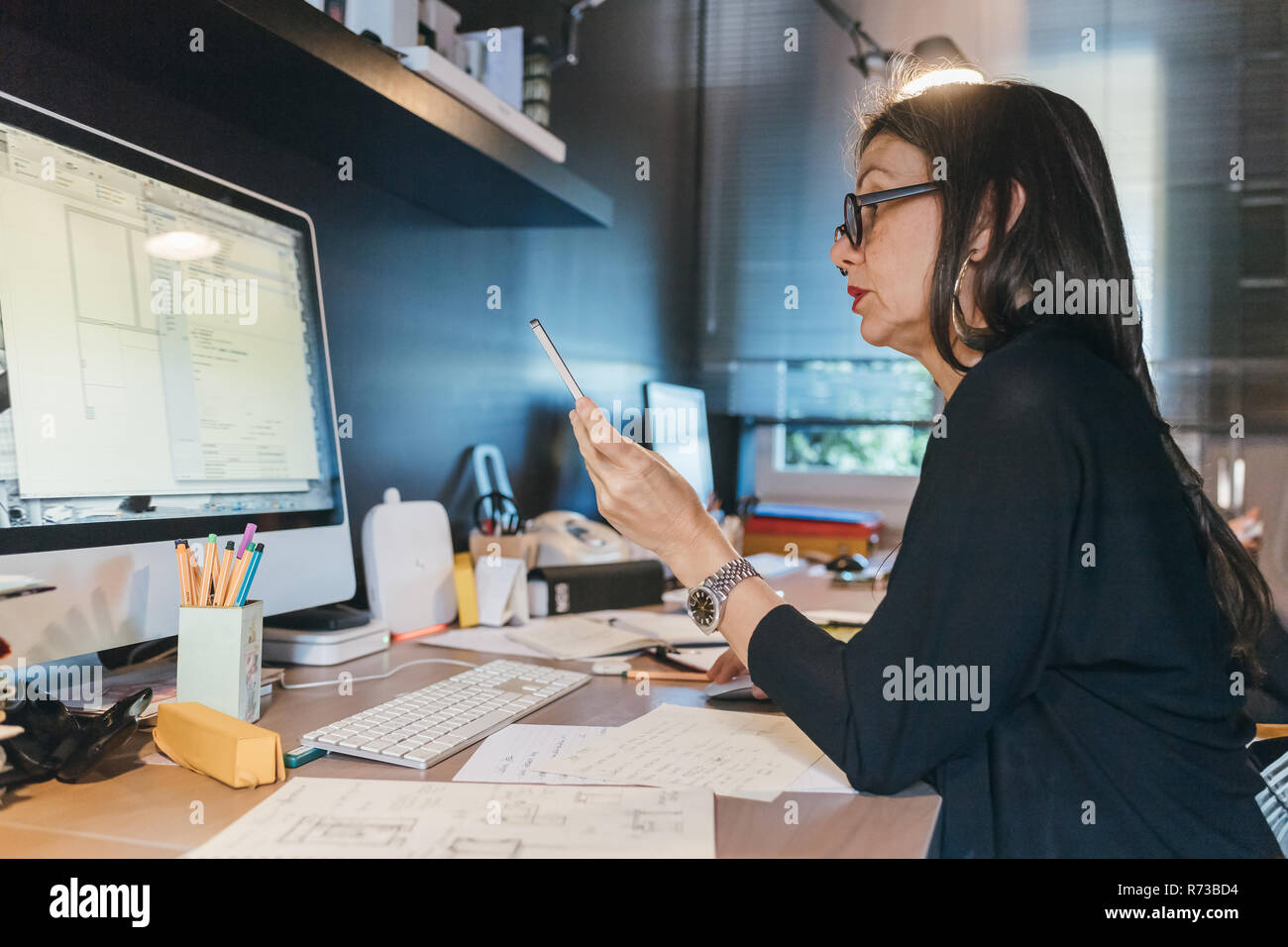 Woman using cellphone at desktop Stock Photo