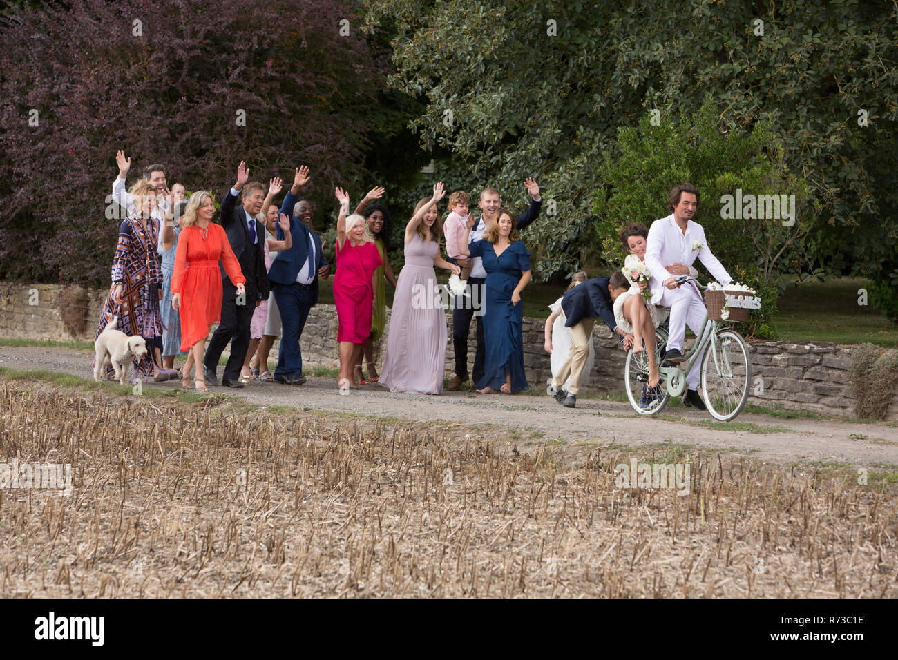 Wedding guests waving off newlyweds on bicycles Stock Photo