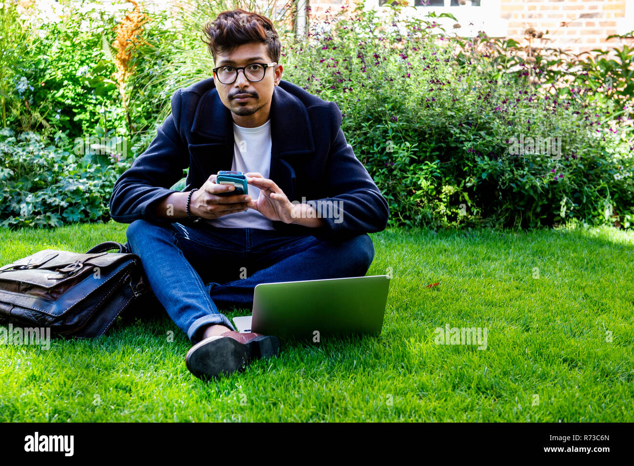Businessman using smartphone and laptop on grass Stock Photo