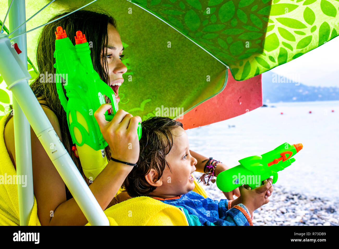 Woman and boy playing with water pistols on beach Stock Photo
