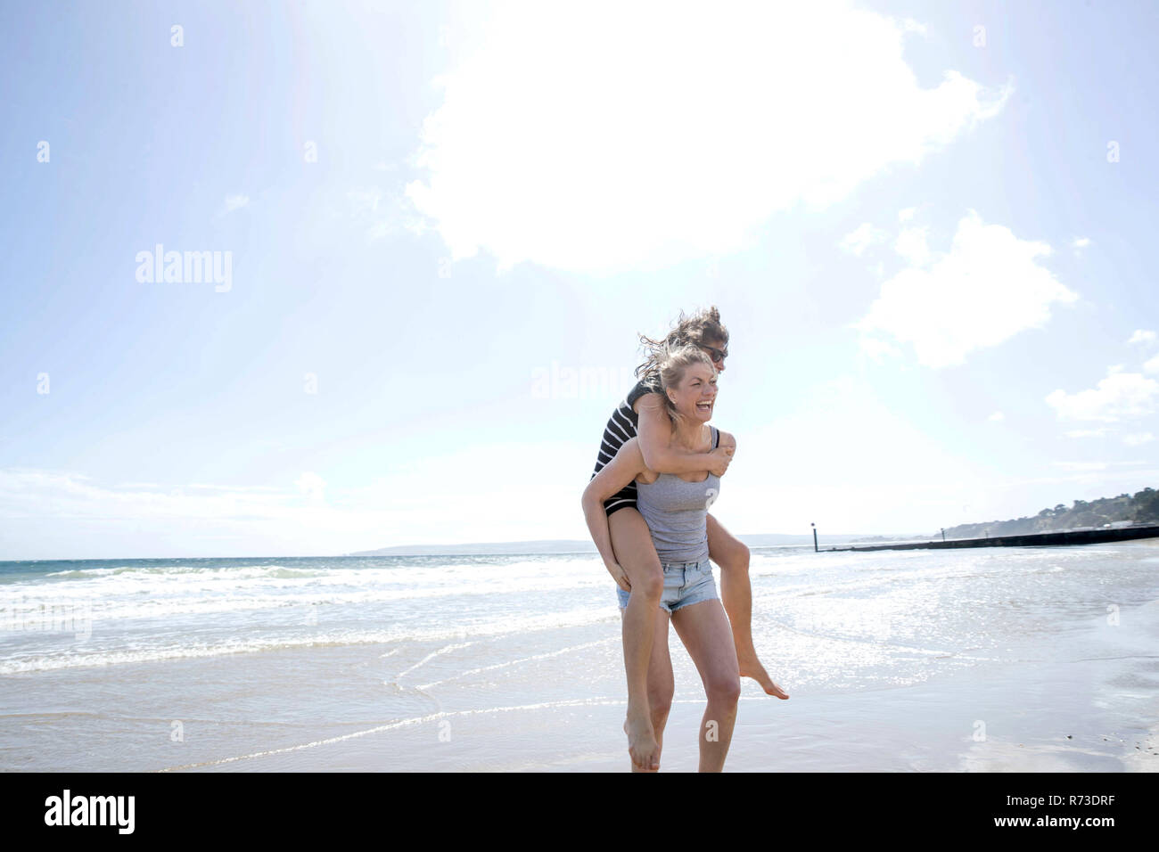 Sisters playing piggyback on beach Stock Photo