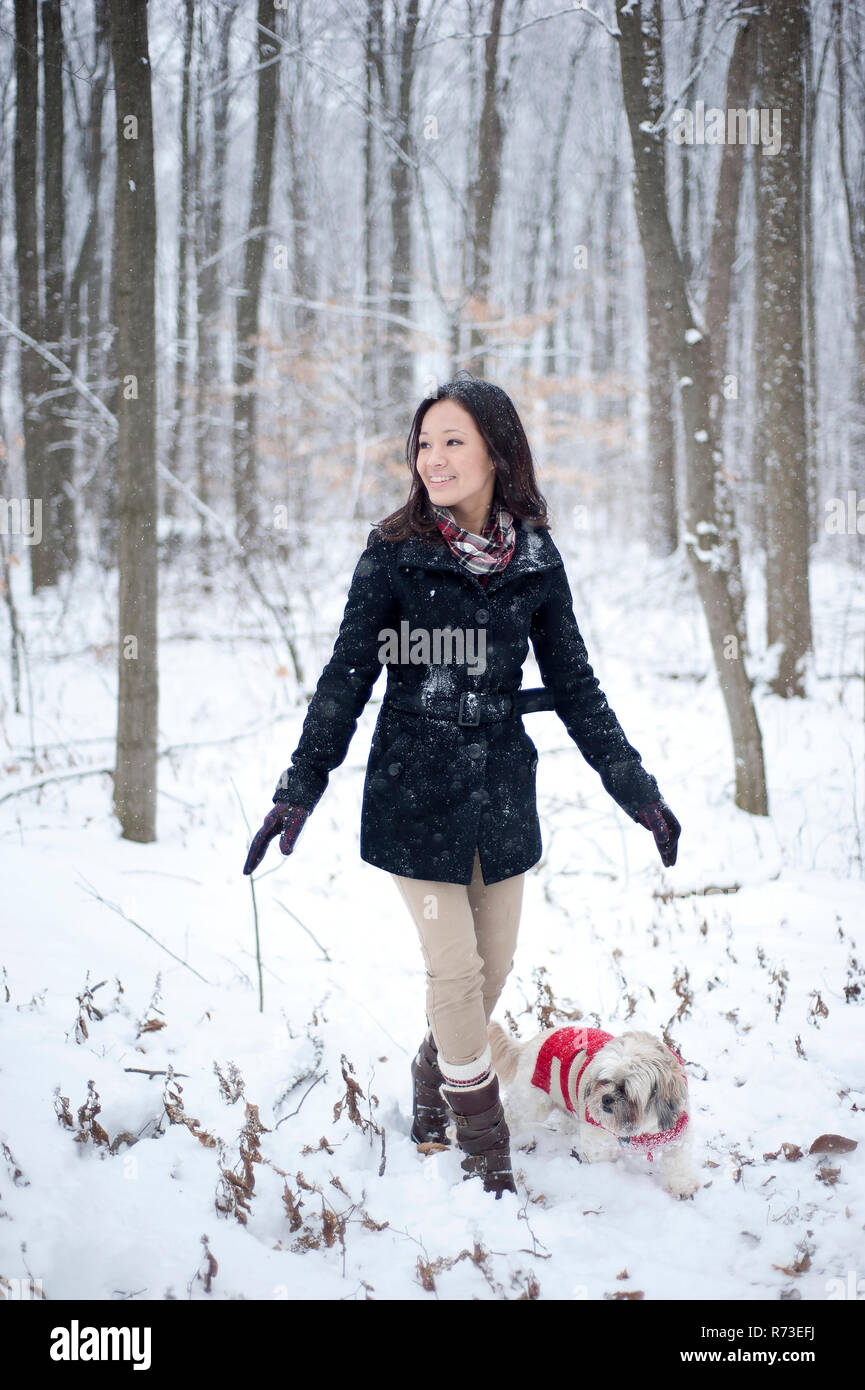Young woman walking dog in snow covered forest, Ontario, Canada Stock