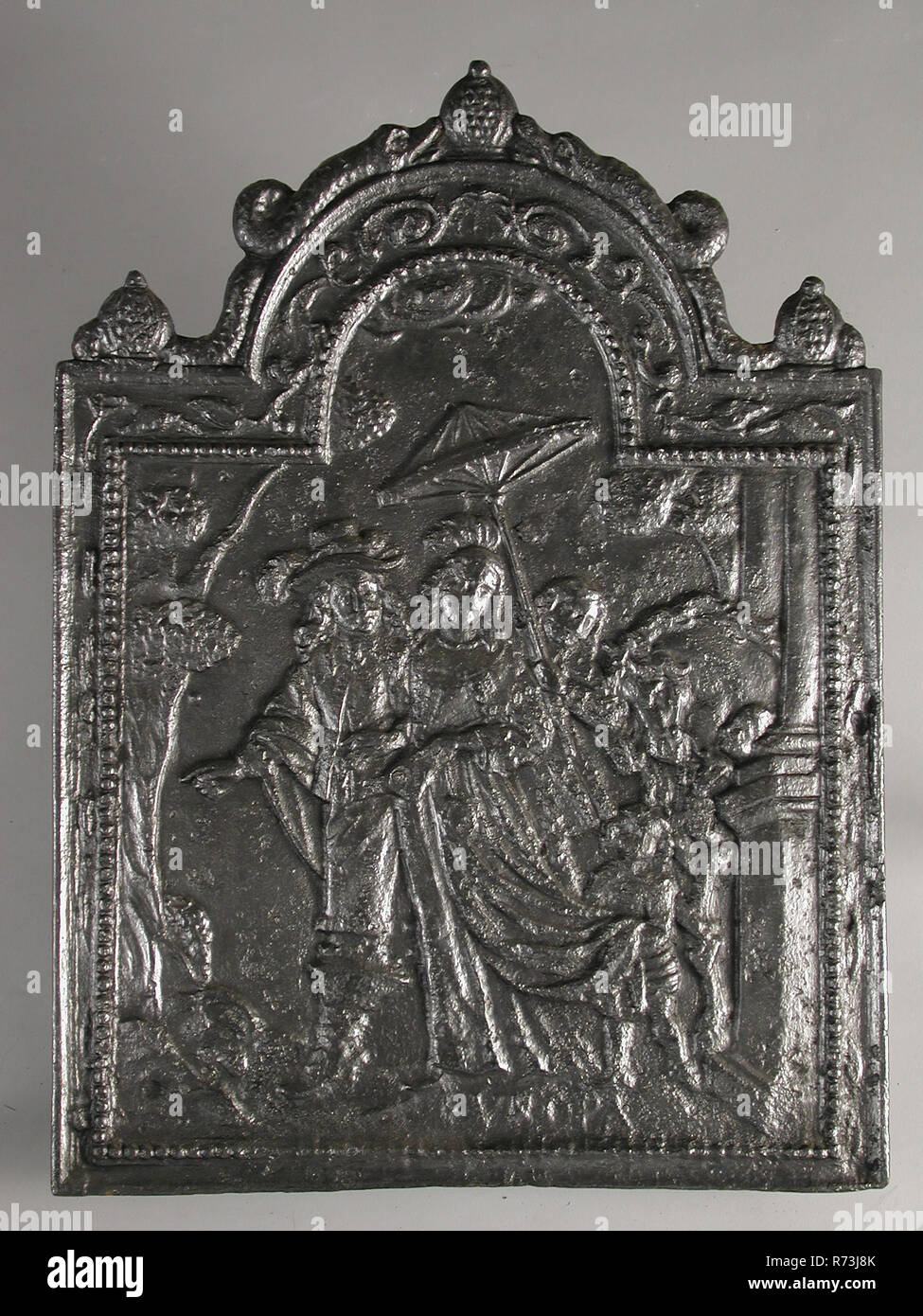 Fireback couple with two children, text Europe, fire place, Rectangular with arch at the top. On top of pomegranate flanked by two dolphins Wide border between frame and pearl necklace in which leaf decoration In the middle image of man and woman in 17th century clothing by column and tree The woman has fan in the left hand. Two servants: one holds the man's cloak and the other holds the parasol over the woman's head. On the side horse with float At the bottom: EUROPA living environment interior heating Occident culture difference Europe Stock Photo