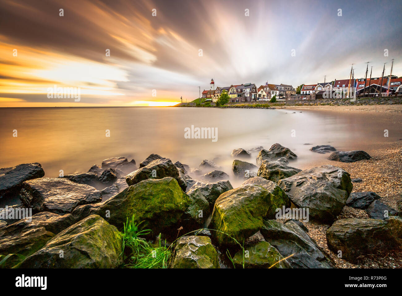 Lighthouse and village of the former Island of Urk alongside the lake IJsselmeer, long exposure with smooth water and dynamic sunset in the Netherland Stock Photo