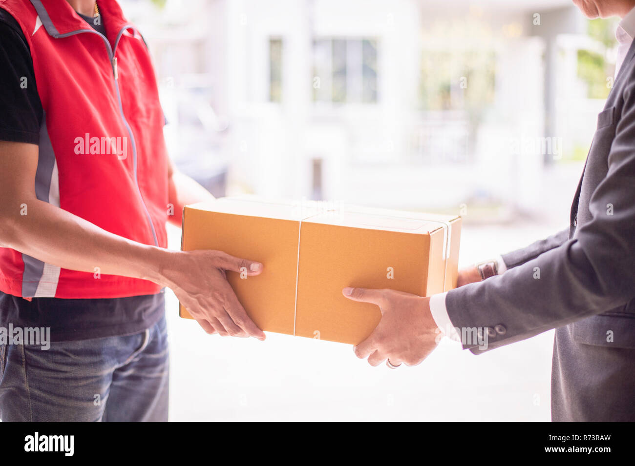 Deliveryman holding the box. A closeup of delivery service staff handing the parcel to man customer at door. Business and logistic concept. Stock Photo