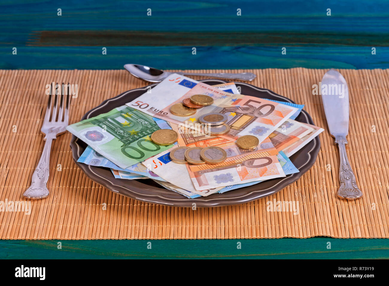 A plate full of money ready to be eaten with cutlery on top of an Asian tablecloth. Stock Photo
