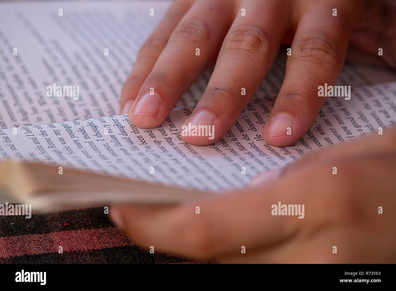Female hands hold open her paperback book as her fingers guide her reading. Stock Photo