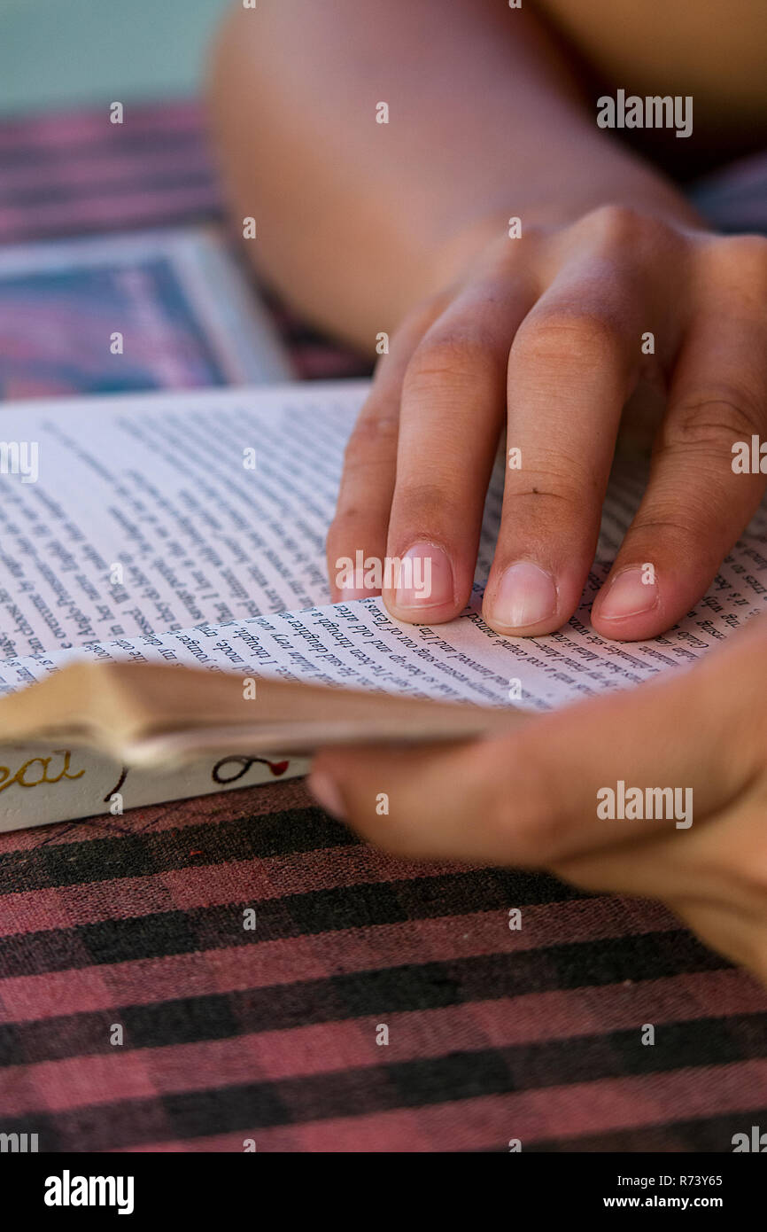 Female hands hold open her paperback book as her fingers guide her reading. Stock Photo