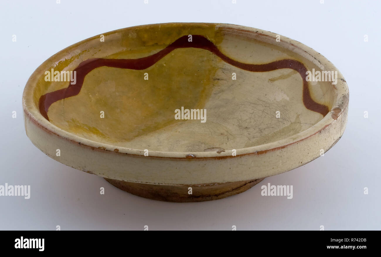 Small earthenware plate, yellow glazed with brown garland along the edge, plate crockery holder soil find ceramic earthenware glaze lead glaze, hand-turned glazed decorated fried lemonade Pottery plate simply decorated in sludge technique Sloping sidewall upright straight edge of board just above the standing surface widening of the bottom Internal yellow glazed along the edge winding brown line underside unglazed Standing surface with subtraction traces. Restoration is not painted on the correct color archeology underground pit Rotterdam City center Stadsdriehoek Oostplein Groenendaal indigen Stock Photo