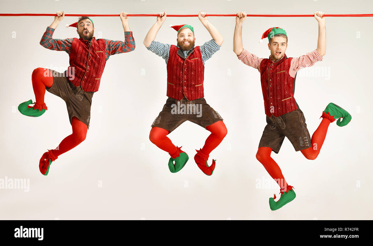 The happy smiling friendly men dressed like a funny gnome or elf hanging on an isolated gray studio background. The winter, holiday, christmas concept Stock Photo