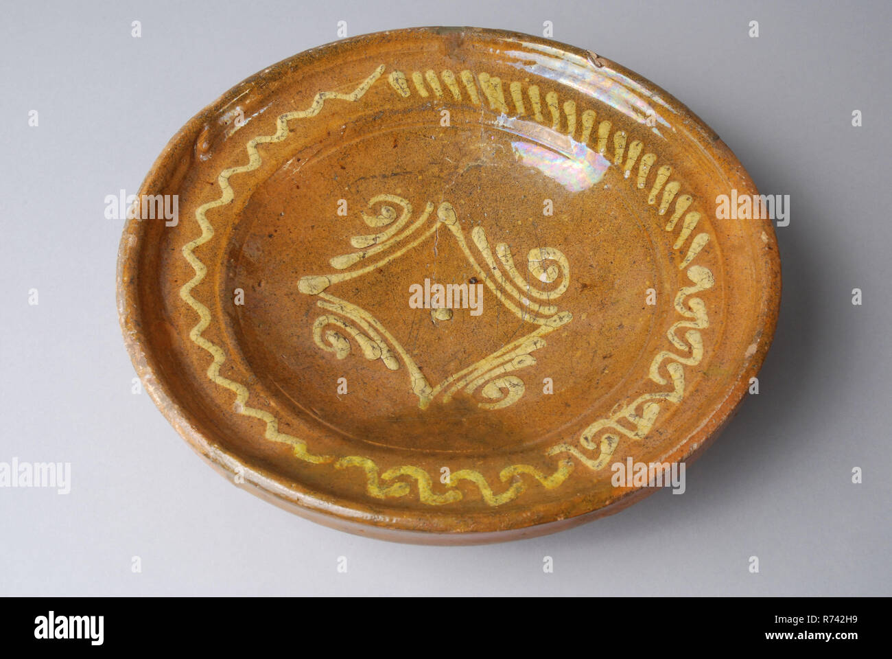 Pottery dish on stand ring, yellow silt decoration in mirror and on the flag, dish crockery holder soil find ceramic earthenware glaze lead glaze clay, hand-turned glazed decorated baked lemonade Pottery saucer on stand ring Glazed internally Decorated in sludge technique Decoration consists of yellow square in the mirror with curved sides some curls and lines On the flag single wavy line short slashes and series of waves Groove and nod on the transition from sidewall to flag narrow flag. Thickened upstanding dish edge. Restoration is repainted archeology underground pit Rotterdam City Triangl Stock Photo