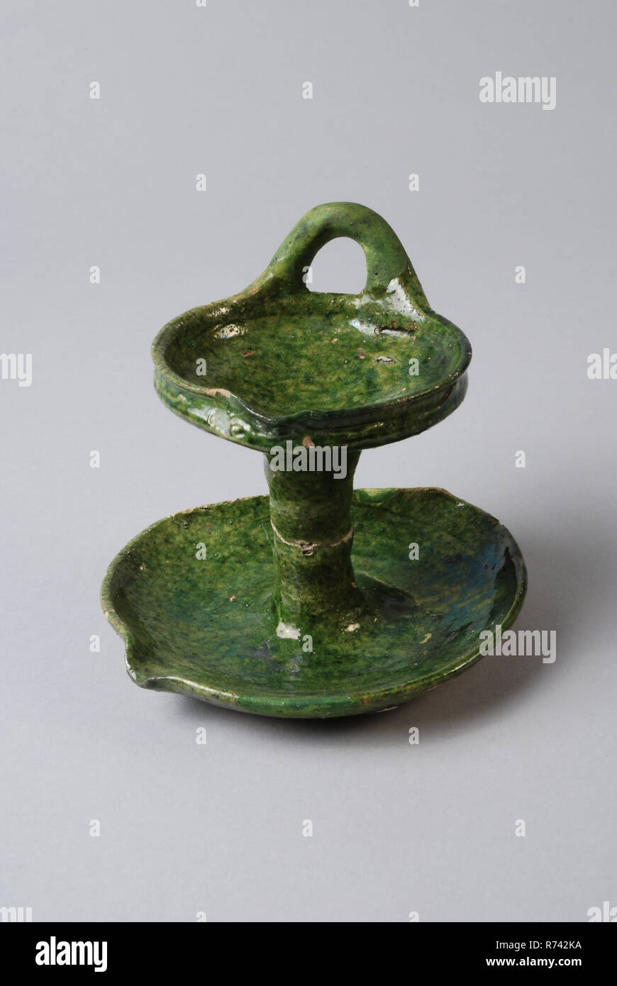 Green earthenware oil lamp with pouring lip and standing ear, two bowls with column between them, oil lamp lamp illuminant soil find ceramic earthenware glaze, hand turned glazed baked Green glazed oil lamp. White shard Two bowls connected by trunk Smaller upper shell with hanging ear and pouring clip Schenklip shell placed more to the side Outstretched soul at the bottom under the column Restoration is painted on color archeology lighting indigenous pottery illuminate oil lamp sleeping evening night Stock Photo