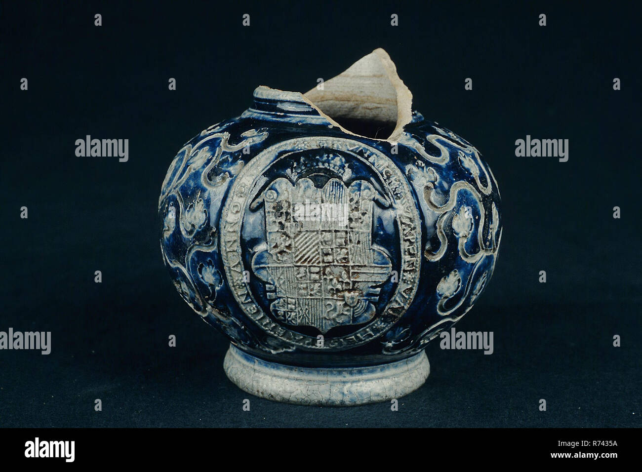 Fragment stoneware bell jar with crowned coat of arms in medallion, sgraffito and blue glaze, Bullet chuck jug crockery holder soil find ceramic stoneware glaze salt glaze, hand turned stamped molded sgraffito glazed baked stoneware bulletbelly dark gray shard with salt glaze short pointed tail around the weapon medallion: KUNNICK. WEAPON OF HEISSPAENIEN. ANNO. (date missing) archeology heraldry import pottery serve serve serve drink wine beer king Hispanje Spain Stock Photo