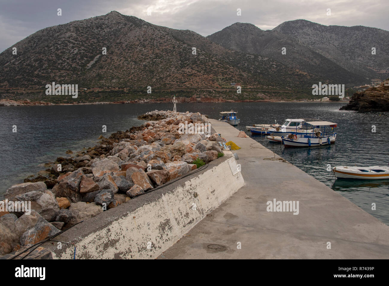 Pier in forefront with some local fishing boats and mountains in background, picture from Bali area in Rethymno on Crete Island. Stock Photo