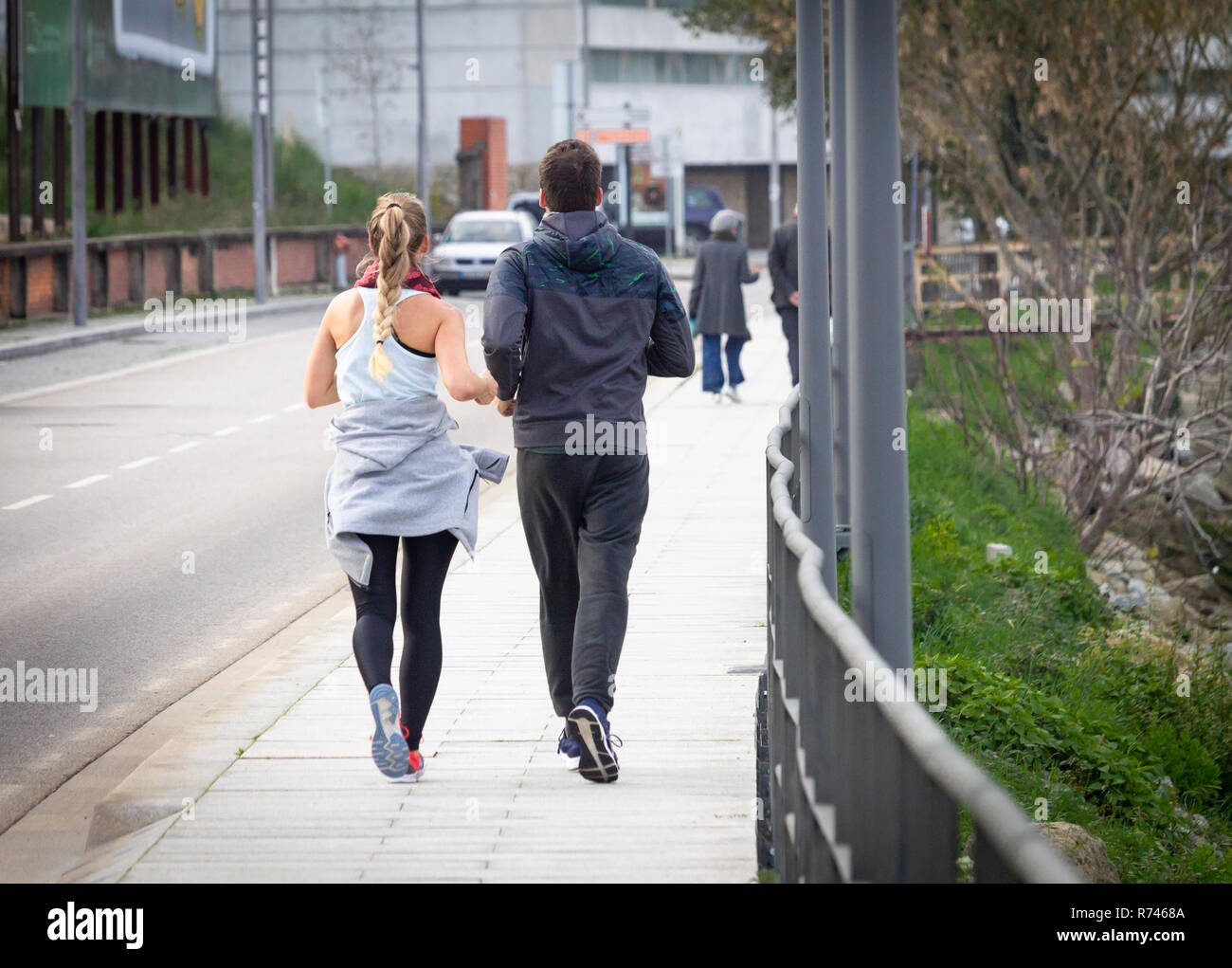 Young couple runs near a paved road. Blonde ponytail girl and tall man. Rear view. Stock Photo