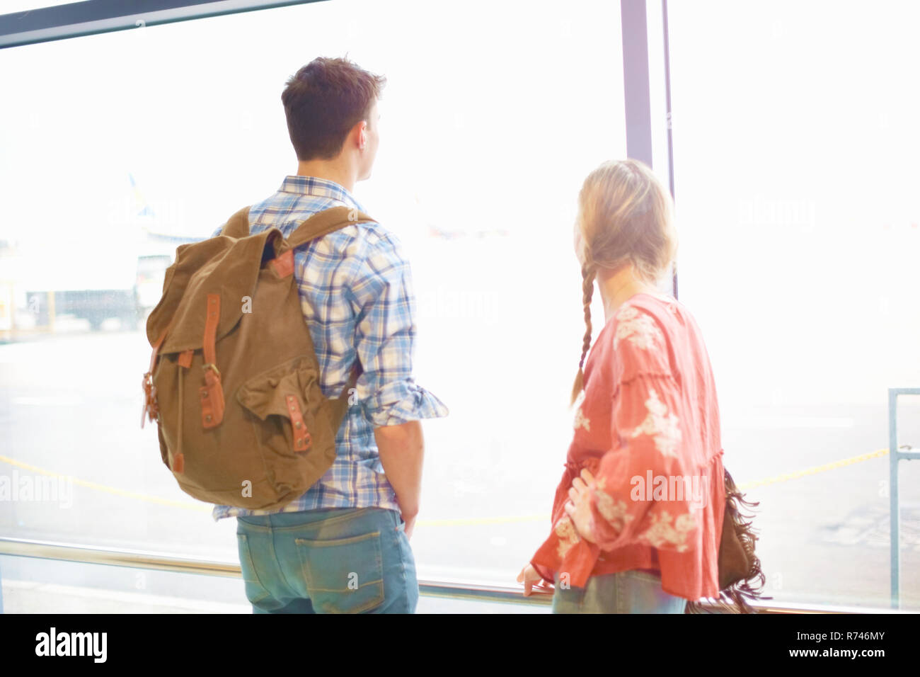 Young couple at airport, carrying backpacks, looking out of window Stock Photo