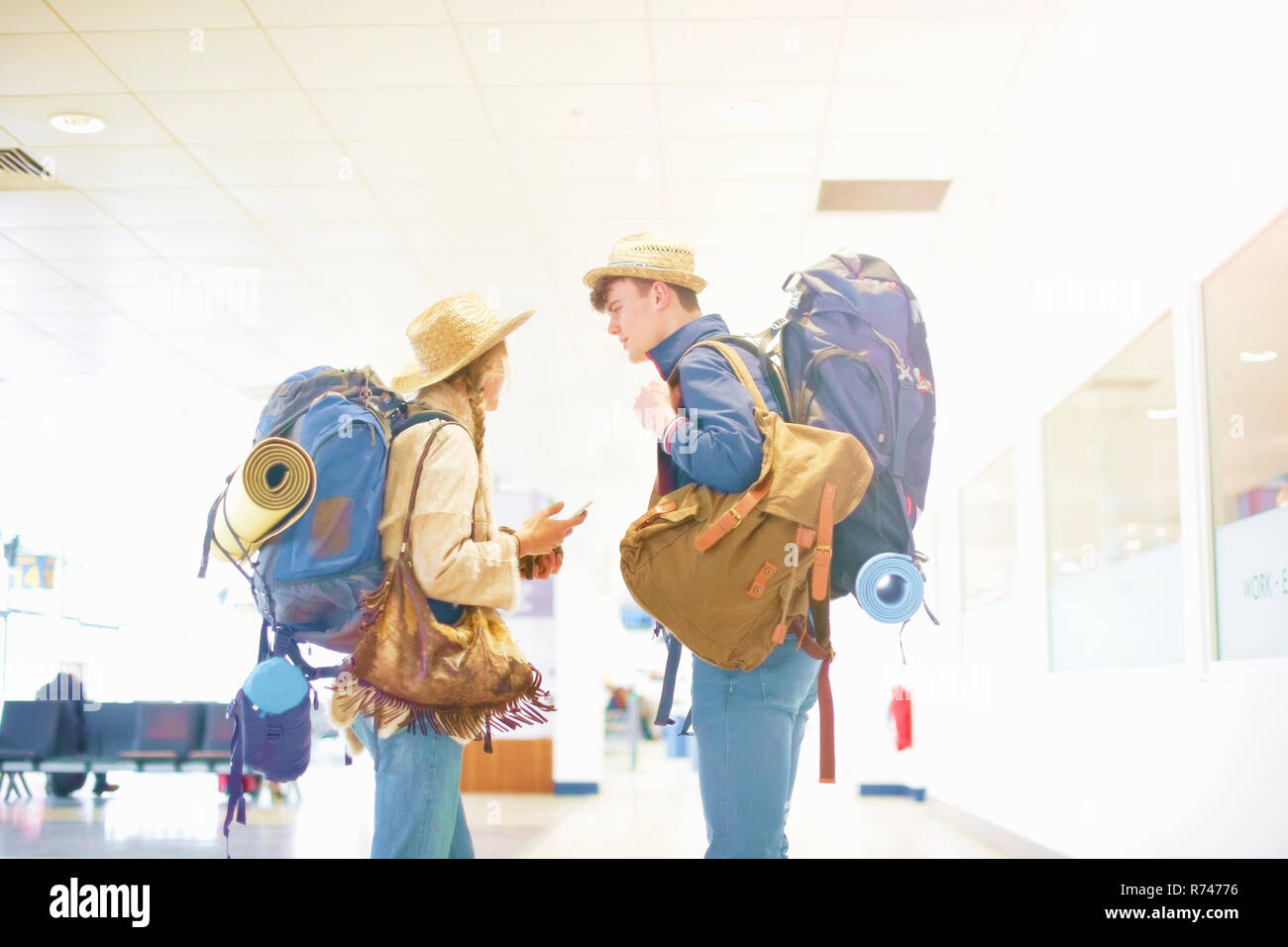 Young couple at airport, carrying backpacks, standing face to face, talking Stock Photo