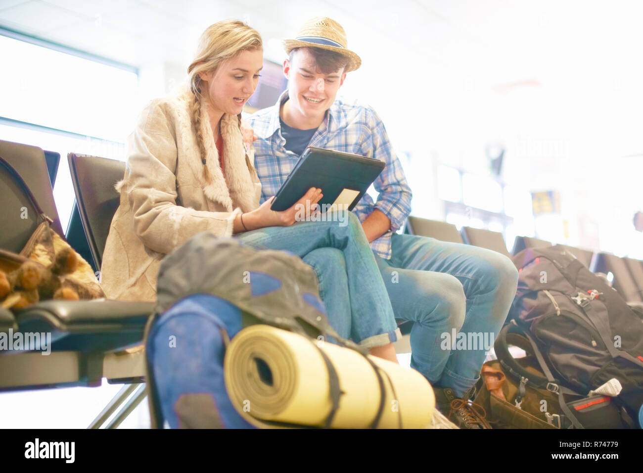 Young couple at airport, sitting, surrounded by backpacks, using digital tablet, low angle view Stock Photo