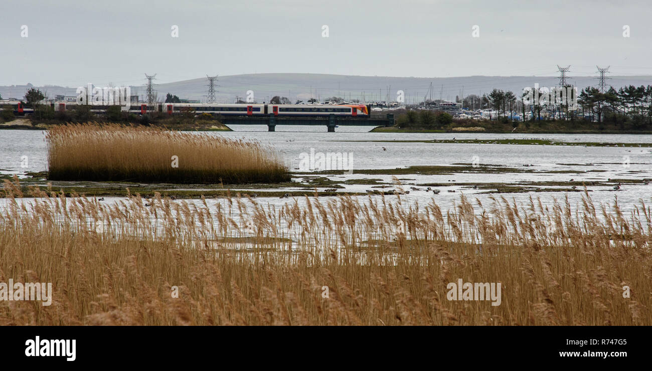 Poole, England, UK -March 17, 2017: A South Western Railway passenger train crosses Holes Bay nature reserve in Poole Harbour in Dorset. Stock Photo