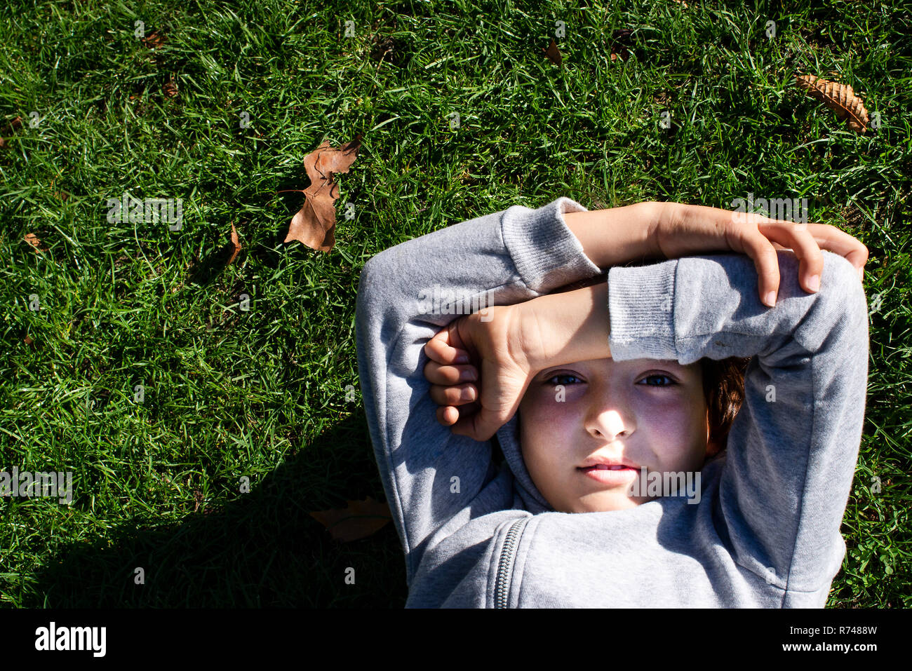 Boy on grass blocking sunlight with arms Stock Photo