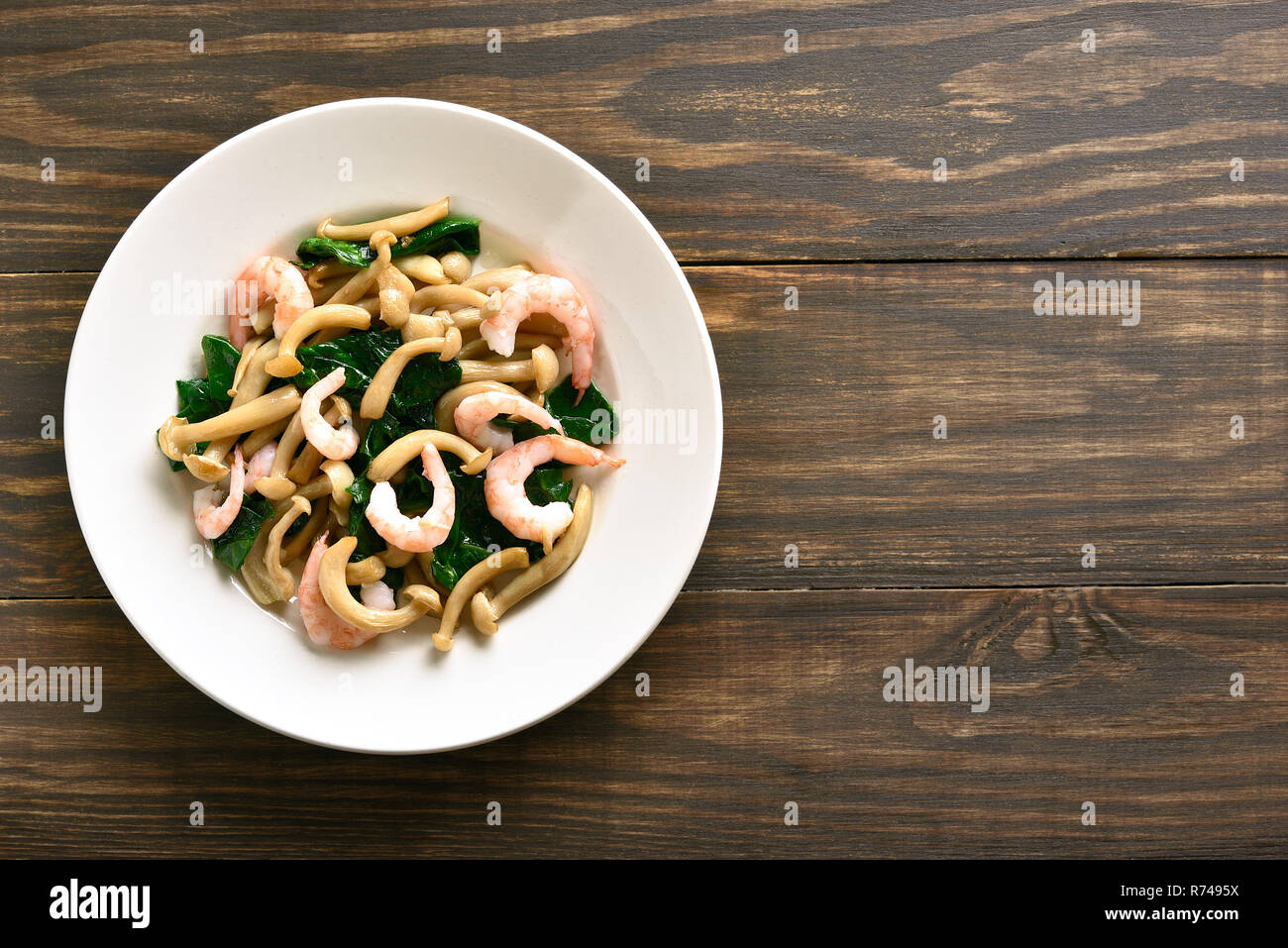 Cooked white beech mushrooms with leaves of spinach and shrimps on wooden background with copy space. Top view, flat lay Stock Photo