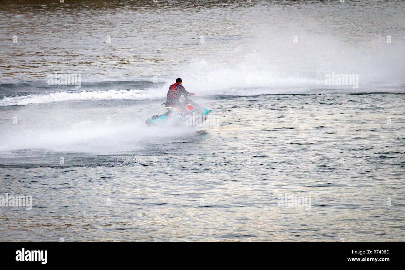 A light blue speedboat with one male rider, speeds along the river. Rear view. Stock Photo