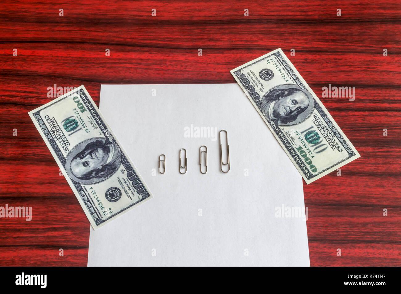 paper clips arranged by size between 100 and 1000 dollar bill on a sheet of paper stock photo alamy