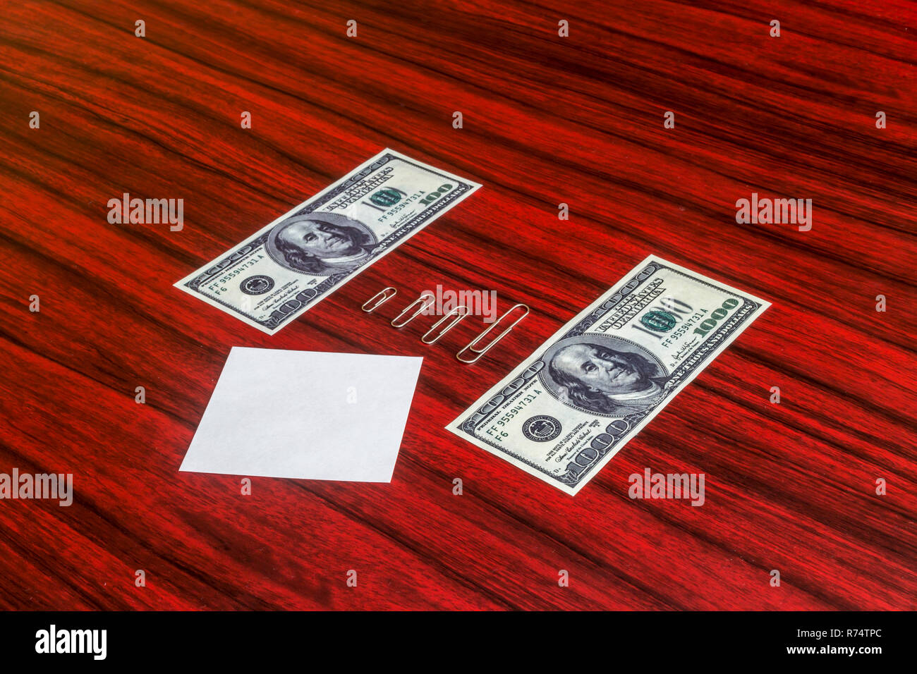 Paper clips arranged by size between 100 and 1000 dollar bill Stock Photo