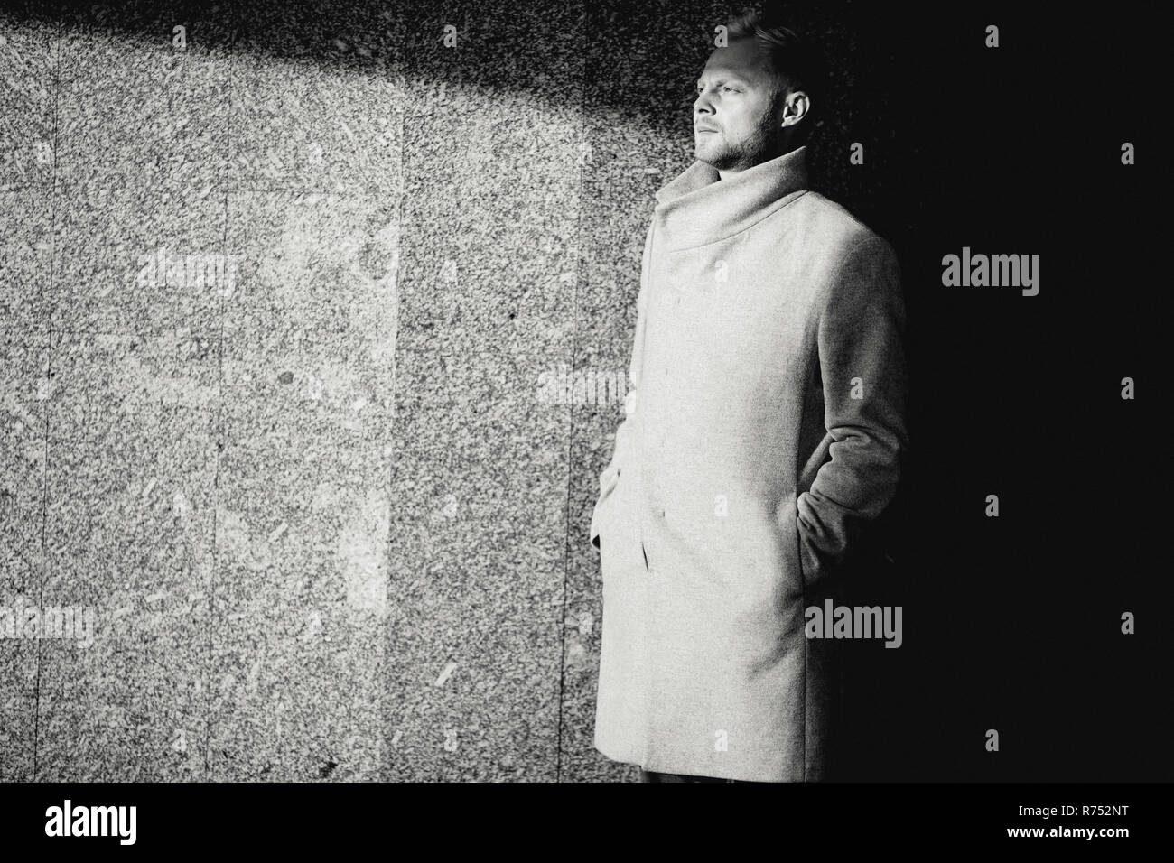 Black and white photo of man in coat walking near wall, defocused background. Stock Photo