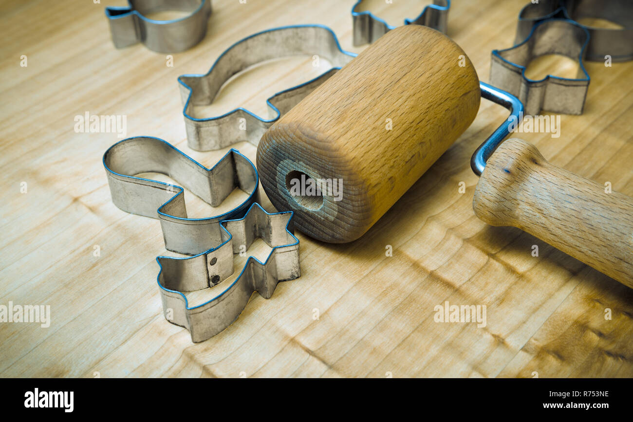Kitchen utensils for preparing Xmas gingerbreads. Still life with a small rolling pin for dough. Metal cutters of various shapes on wood pastry board. Stock Photo