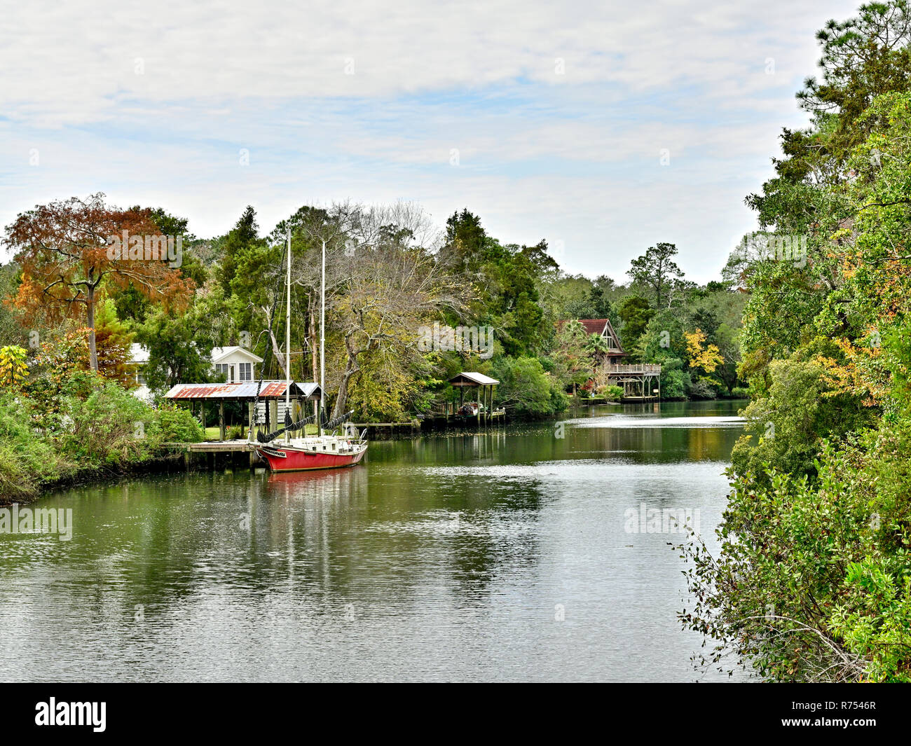 Single red sailboat tied up to a small dock on the Eslava Branch or bayou in South Alabama, USA. Stock Photo