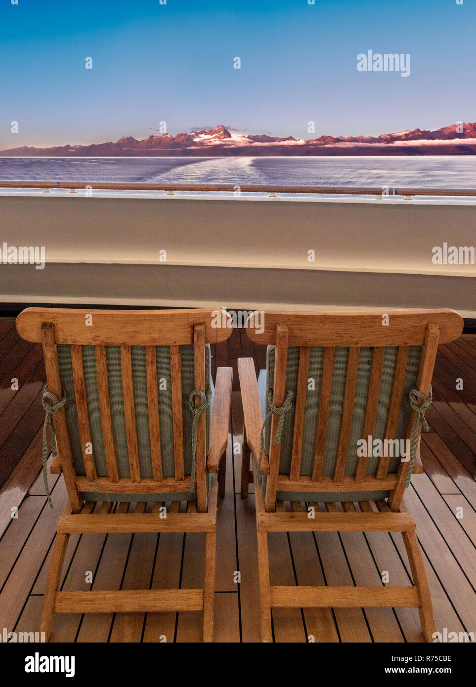 Pair of two cruise ship wooden lounge chairs facing dawn sunrise on sea and mountains. Near