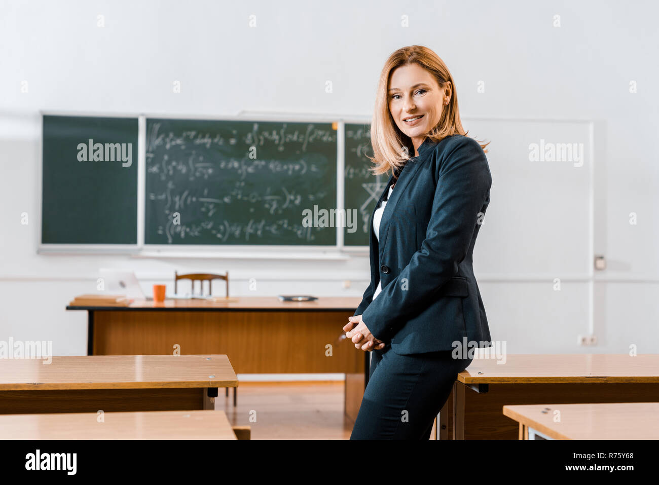 beautiful female teacher in formal wear smiling and looking at camera in  classroom Stock Photo - Alamy