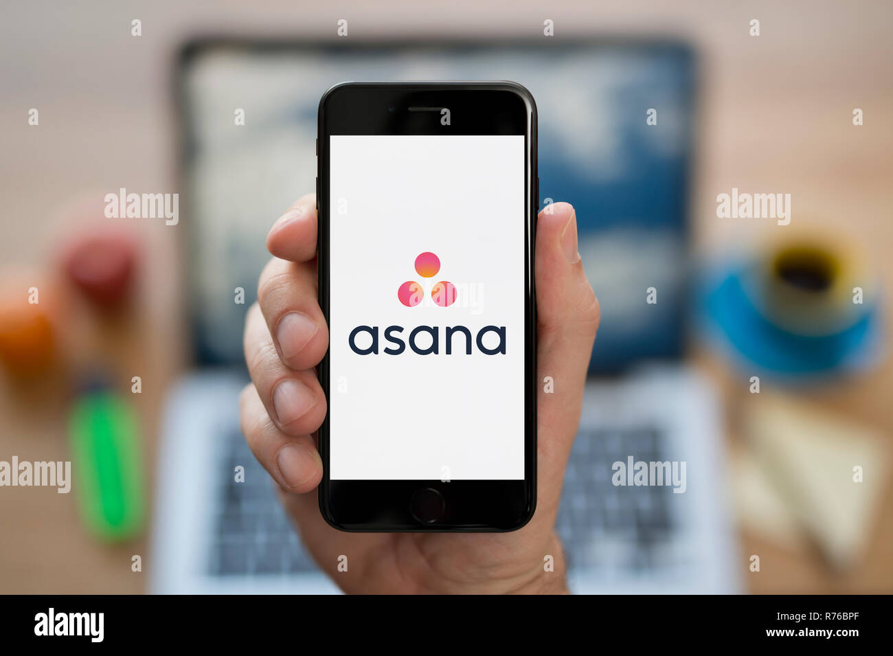 A man looks at his iPhone which displays the Asana logo (Editorial use only). Stock Photo