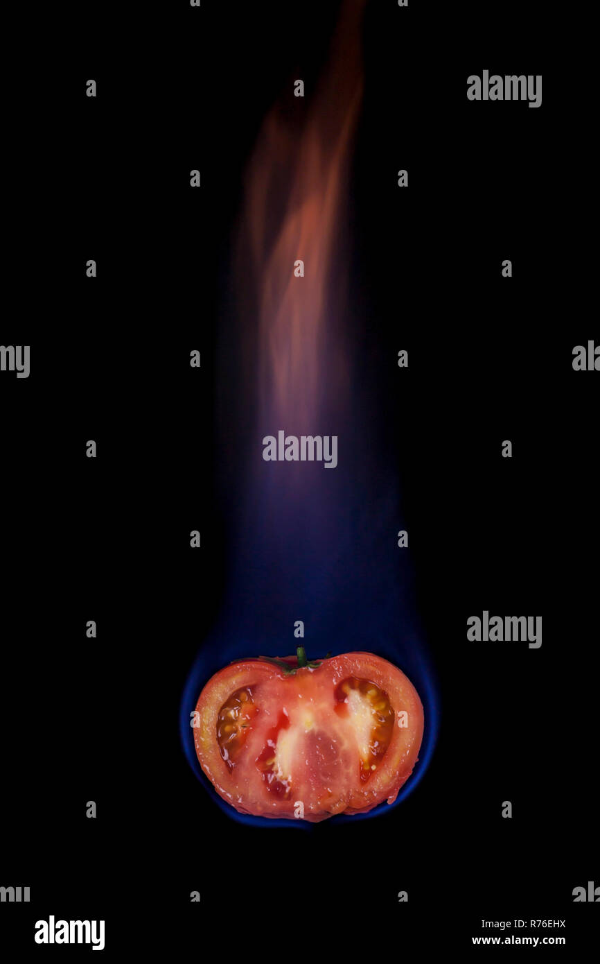 Tomato on fire with blue flames isolated on black background Stock
