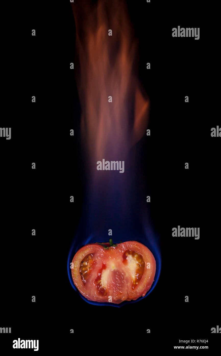 Tomato on fire with blue flames isolated on black background Stock