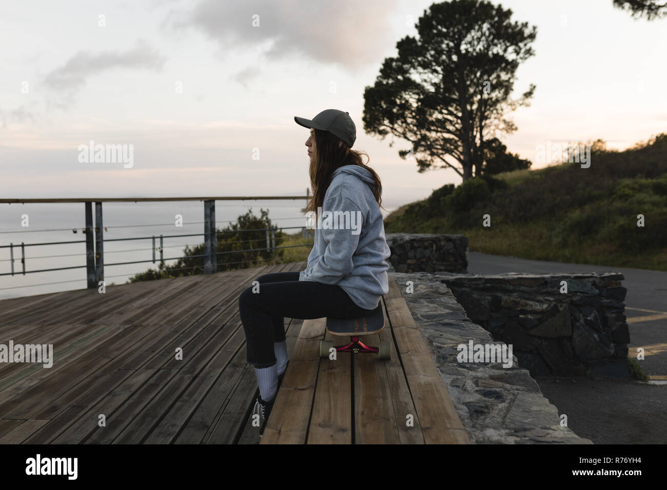 Female skateboarder sitting on skateboard by railing at observation point Stock Photo