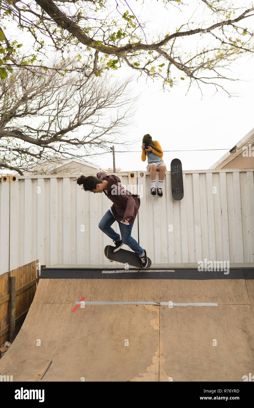 Female skateboarder clicking photo while male skateboarder skating on