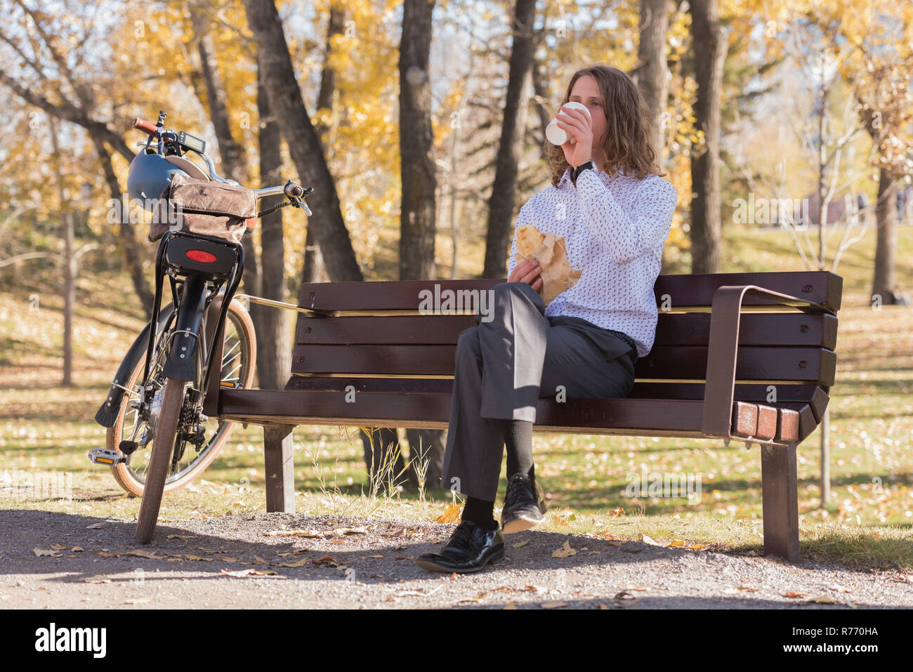 Man having coffee while sitting on a bench in the park Stock Photo