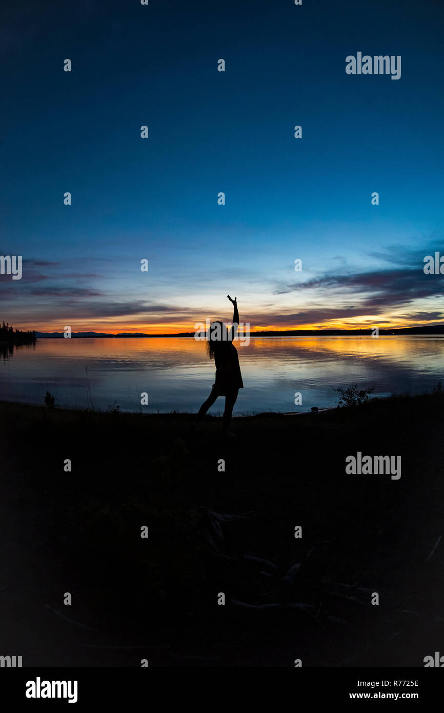 Wide angle image of silhouetted woman standing by the water, stretching