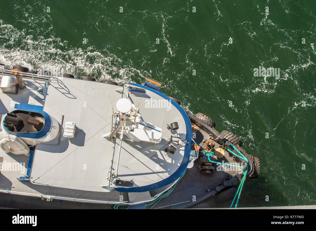 Overhead POV view of tugboat, ropes and workers assisting large ship to dock in high winds on a bright sunny day. Gastineau Channel, Juneau, Alaska, U Stock Photo