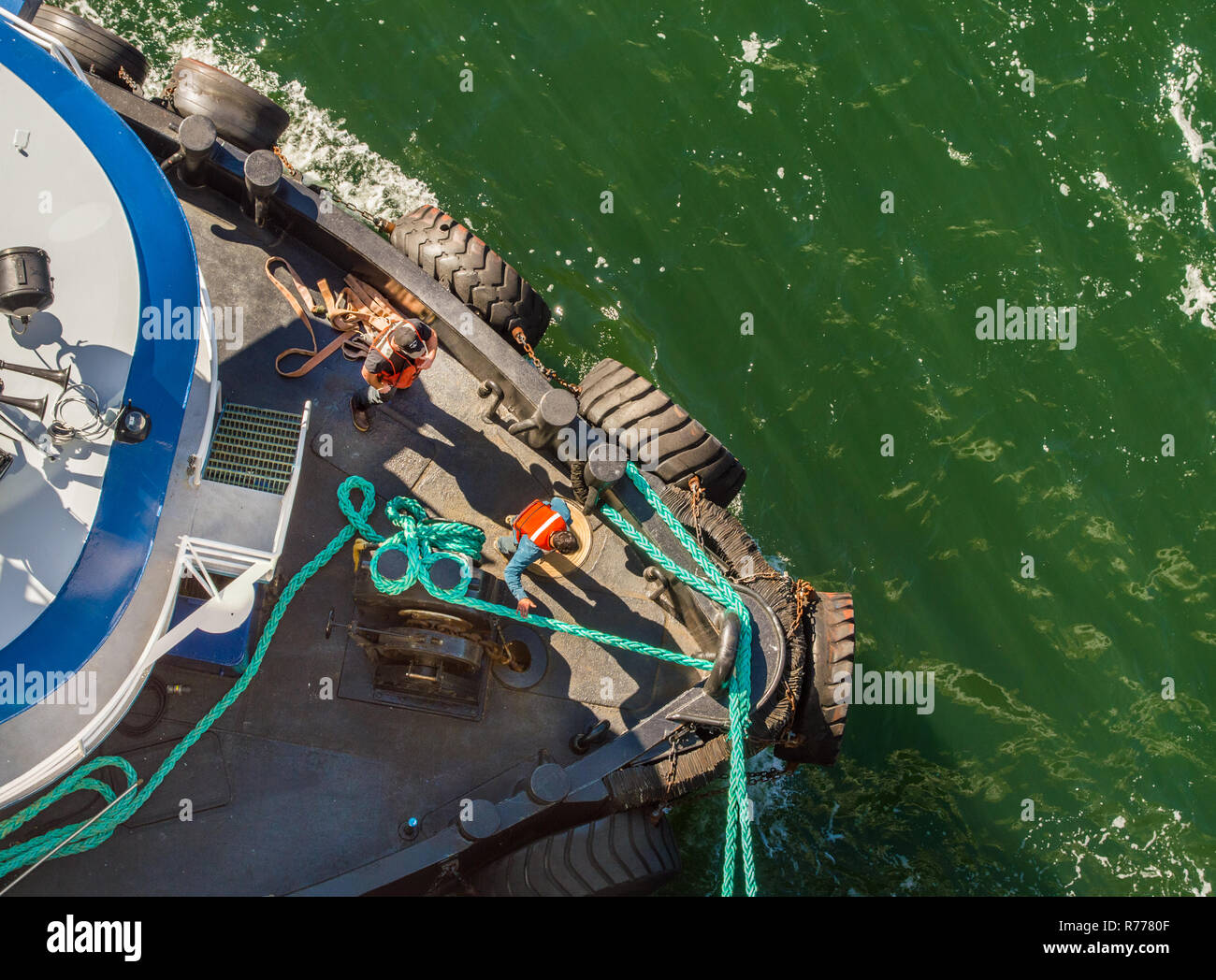Overhead POV view of tugboat, ropes and workers assisting large ship to dock in high winds on a bright sunny day. Gastineau Channel, Juneau, Alaska, U Stock Photo