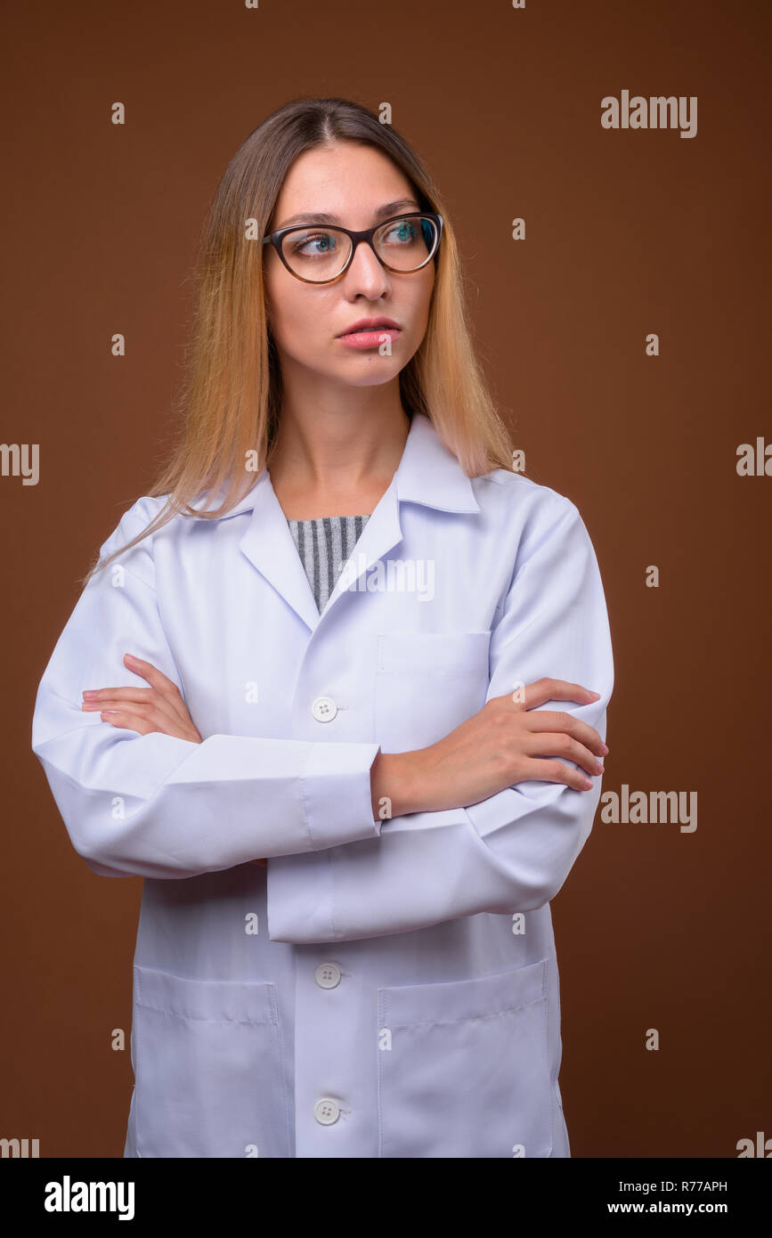Portrait of young beautiful woman doctor thinking against brown ...