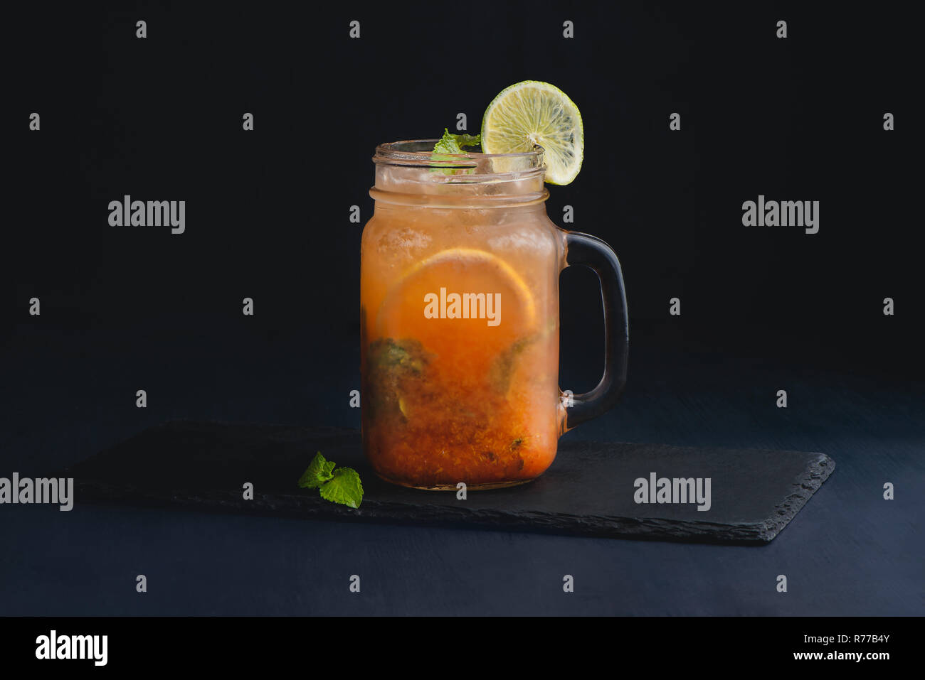 Ice cold citrus cocktail in a vintage glass mason jar. Dark background with copy space for a menu. Stock Photo