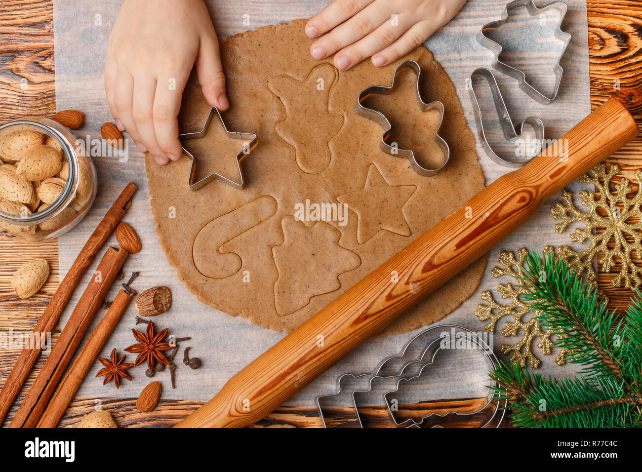 Baby's hands makes traditional gingerbread. Spices on the table-anise, cardamom, cinnamon, cloves, nutmeg, almonds. Raw dough and clippers in the form Stock Photo
