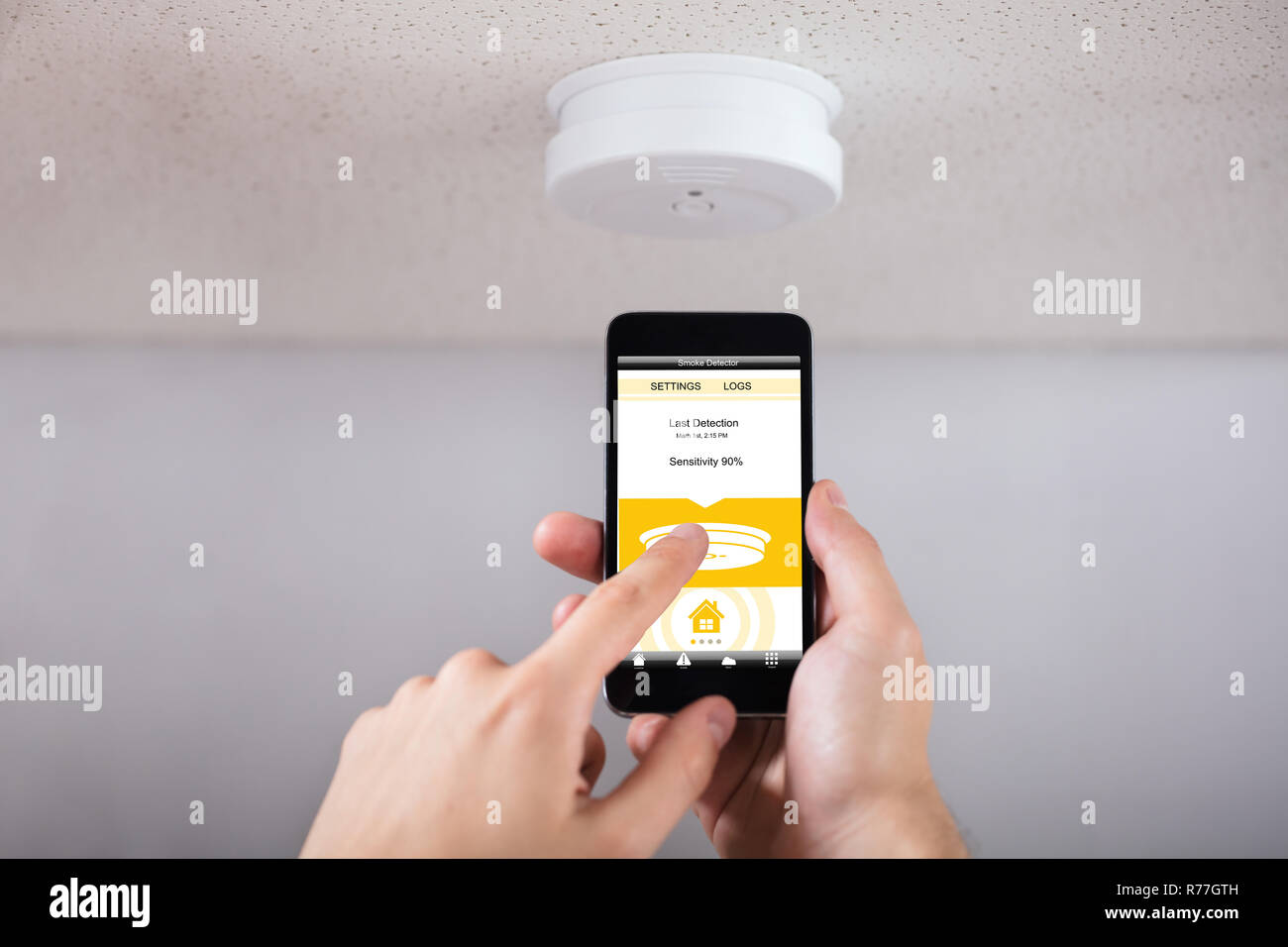 Person Operating Smoke Detector With Mobile Phone Stock Photo