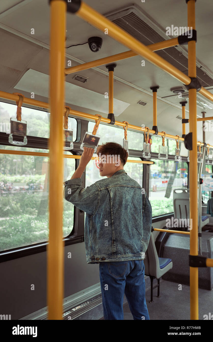 Young cheerful handsome man is holding onto the bar while standing in a bus. Stock Photo