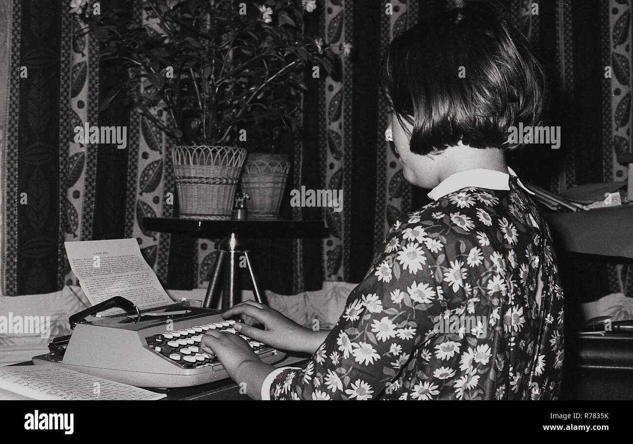 1970s, young girl in a flower patterned top sitting at a desk typing up her notes neatly on a small manual typewriter, England, UK. Stock Photo